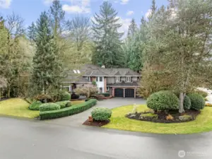 A stately curbside view showcasing this elegant residence set on a quiet circular drive, framed by mature evergreens and manicured landscaping. The classic architecture, brick accents, and lush grounds create a timeless, private estate-like presence.