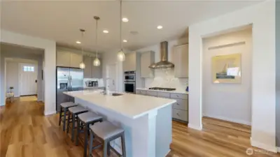 Spacious modern kitchen with quartz counters, large island, stainless steel appliances, double ovens, 5 burner gas cooktop, pantry, and abundant cabinetry.