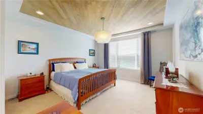 Spacious primary bedroom with wood-accent tray ceiling, elegant lighting, and abundant natural light.