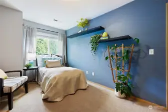 The same 3rd bedroom in the daylight, showcasing the rich deep blue accent wall and green view out of the window.