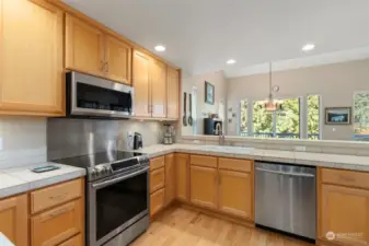 The kitchen enjoys high-end stainless appliances, hardwood floors, and a view of the trees beyond.