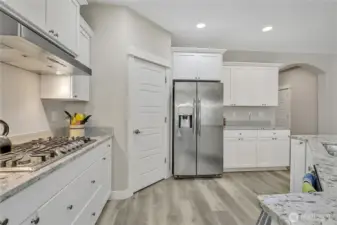 All white cabinetry, stainless steel appliances, a pantry, and a large center island add to the appeal of this kitchen.