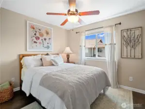This bright and tranquil bedroom offers a welcoming atmosphere, complete with a large window for natural light and a ceiling fan for comfort.