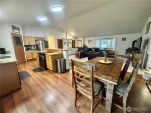 From the dining room, straight ahead is the living room. To the left is the kitchen, and to the left of the kitchen is the doorway to the deck. This entire area has a vaulted ceiling and Luxury Vinyl Planking.