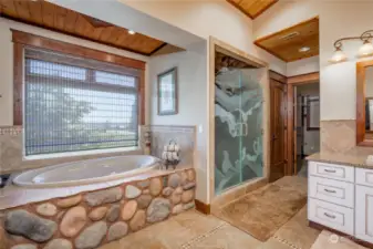 The river rock jetted tub, adjacent to the walk-in shower.  Notice how the wood soffit ceilings enhance and provide warmth to the area.  The walk-in shower has art glass design doors