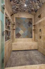 The walk-in shower features 6 wall mounted jets, 4 ceiling jets and a hand-held shower wand, artistic tiling, and an arched river rock ceiling