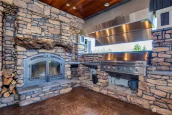 The outside covered porch fireplace and barbecue area, with professional grade appliances and rock walls.  Notice also the burl wood fireplace mantle and wood soffit ceiling, with recessed can lighting