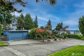 The approach to 4221 W Armour is as dignified as the residence itself—ample off-street parking, clean lines, and a double carport discreetly tucked behind sculpted Japanese maple. From this quiet Carleton Park street, the Puget Sound glimmers just beyond the treetops, reminding you that the heart of the Pacific Northwest is always close at hand.