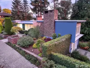 From this elevated southeast vantage, the sculptural composition of 4221 W Armour comes into full view: crisp rooflines, basalt chimney, cobalt stucco, and a tapestry of clipped hedges and flowering beds. A masterwork of site and structure by Tucker & Shields—rooted in the landscape, yet unmistakably modern.