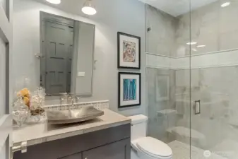 Set away from the open living space, is the main-level guest bath with custom cabinetry, a hammered nickel vessel sink and glass-enclosed walk-in shower.
