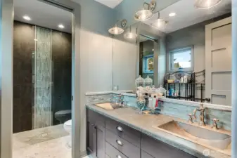 Spacious upper-level bath featuring dual vanities with hammered nickel sinks, custom cabinetry, and a glass-enclosed walk-in shower with designer tilework, thoughtfully designed to serve the oversized guest bedrooms.