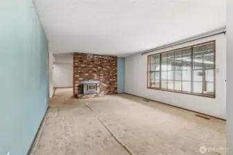View of the living room from the hallway, double-sided fireplace and kitchen straight ahead. Love the large windows!