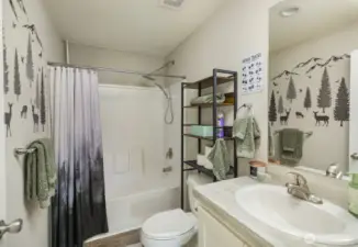 A clean and well-designed full bathroom with tub/shower combo, modern fixtures, and playful nature-themed wall accents for added charm.