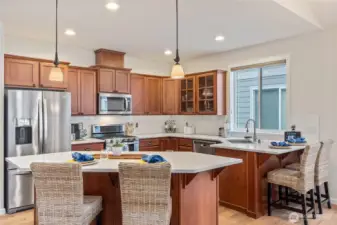Stainless-steel appliances and a generous island with seating make meal prep and casual dining a joy. Pendant lighting and large windows bathe the space in natural light, creating a welcoming atmosphere.