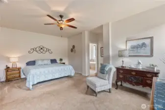 The primary bedroom offers a tranquil retreat with generous proportions and tasteful design. A neutral palette and plush carpeting create a soothing ambiance, while a ceiling fan adds comfort and complements the high ceiling.