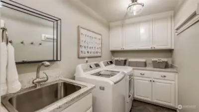 Utility room adorned with quartz countertops, painted cabinetry, updated lighting, and a hidden hanging system mounted on the wall.