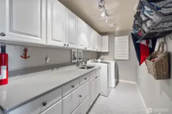Spacious laundry room with a sink and long countertop is between the garage & kitchen