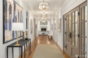 Grand center hall and gallery with freshly paneled walls and ceiling, art lighting, and glass transoms over doorways