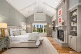 Elegant primary bedroom with soaring ceilings, built-in bookcases, a two-sided fireplace and a peek-a boo view of Seattle