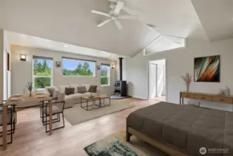 Abundant natural light and magnificent views of the landscaped grounds and surrounding forest create a serene atmosphere. Custom wall sconces complement the free-standing wood stove, which features a built-in fan, while the ceiling fan helps circulate warmth throughout the space. To the right, the attached bath boasts a large closet, an 8.5-foot walk-in shower with dual shower heads, a built-in bench, and custom tilework.