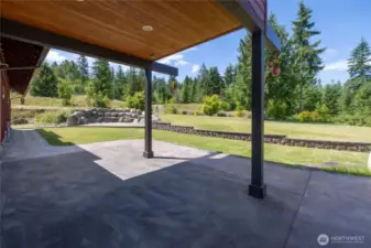 This view highlights the upper-level balcony, which provides a shaded patio area below—perfect for relaxing on warm days. A block wall elegantly separates the patios from the expansive, landscaped yard, which features a sprinkler system. Additionally, a separate cobblestone patio bordered by a striking large rock wall offers an ideal space for a fire pit and outdoor gatherings.
