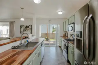 This stunning kitchen showcases custom butcher block countertops, under-cabinet lighting, stainless steel appliances, a large sink, and a breakfast bar for guests—plus easy access to the back deck through the sliding glass door.