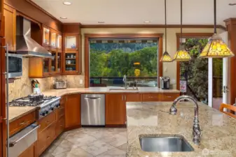 Kitchen features a gas cooktop, prep sink, warming drawer, and lighted display cabinetry, with granite surfaces and a picture window framing peaceful river and mountain views.