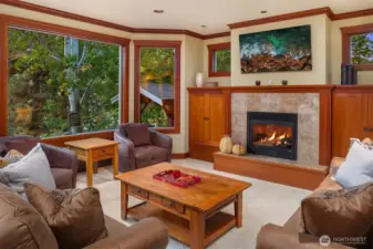 Cozy secondary living area with fireplace and wraparound windows, offering a warm retreat surrounded by peaceful, tree-lined views.