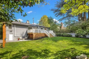 Spacious backyard with lower patio area, upper deck and luscious greenery.