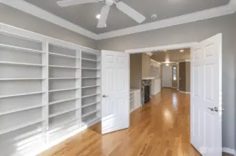 Private den has a wall of built-in shelves, crown molding, ceiling fan and solid private doors.