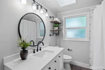 Light and bright, this bathroom features sleek white tiles, stylish black fixtures, a durable vinyl plank floor, skylights, a shiplap ceiling, and a large frosted window ensuring privacy without sacrificing natural light.