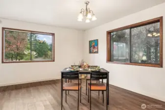 Two large picture windows bring the outdoors in and frame the serene grounds created by privacy trees .  The la ample corner might be the perfect place for your future wood or propane freestanding stove or display cabinet.