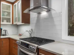 This high-end chef's kitchen features a professional grade gas range sleek designer hood and. timeless subway tile backslash.