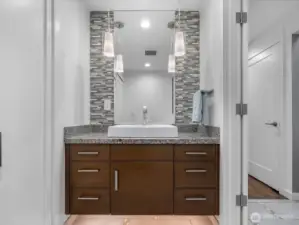 The remodeled powder room exudes refined elegance, featuring a floating vanity with vessel sink, granite countertops, a mosaic tile backsplash, and designer pendant lighting, with a discreetly integrated washer and dryer closet for added convenience.
