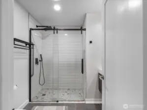 A spa-like updated hall bathroom featuring walk-in shower, with designer pebble tile flooring sleek matte black hardware double sinks for a modern, high-end finish.