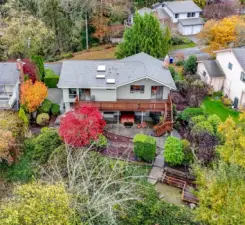 This view shows the new roof, expansive deck with stairs to the lower patio and the .3 acres of serene landscape facing west for spectacular sunset views.