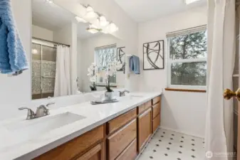 The primary bathroom features updated counters, dual sinks and a glass door, step-in jetted tub/shower combination plus views of the private portion of the lot beyond.
