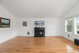 Open living area with gas fireplace & hardwood floors, lots of windows