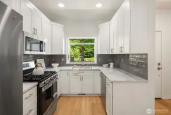 The gorgeous new kitchen boasts white shaker cabinets, a stylish tile backsplash, sleek white quartz countertops, modern fixtures, and stainless steel appliances—including gas cooking—for a perfect blend of elegance and function.