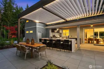 Sprawling chef-style island anchors the outdoor kitchen, with seating for six