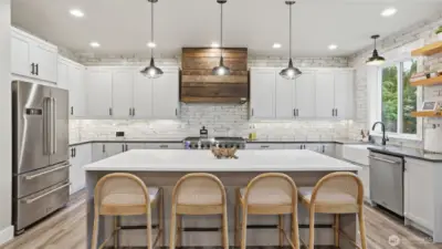 True entertainer’s kitchen with oversized island, custom hood, open shelving, quartz countertops, commercial appliances, walk-in pantry, and wine fridge.