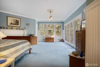 Another view of the primary bedroom, which has large windows and beautiful fireplace mantle.