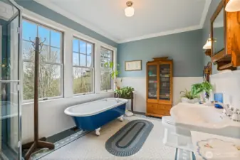 The primary bath is accented beautifully with tile flooring, claw foot bath tub, wainscoting, and vintage lighting.