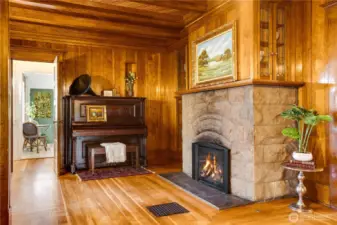 A second original stone fireplace draws the eye beyond the living room into the adjacent den. The homeowners installed a new gas fireplace for comfort. Notice the built-ins with leaded glass doors above the mantel.