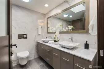 Natural light pours through the remote-controlled skylight, illuminating floating vanities, a dual rainfall shower, and radiant tile floors that keep every step warm and comfortable.