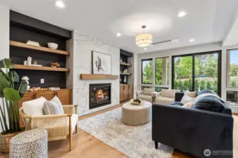 This cozy family room invites relaxation with its plush seating, warm wood accents, and soft neutral tones layered throughout. The geometric-tiled fireplace serves as a stylish centerpiece, flanked by built-in shelves that add charm and functionality. Natural light pours in through large windows, creating a bright yet intimate space perfect for gathering or unwinding.