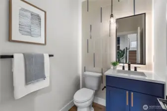 This guest bathroom combines sleek design with thoughtful details, creating a space that’s both stylish and welcoming. The blue vanity adds a pop of color against the neutral tile backdrop, while the backlit mirror and pendant light offer a soft, modern glow. Clean lines, layered textures, and curated accents make it a standout feature for visitors.