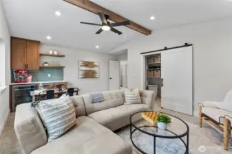 This entertainment room combines relaxed comfort with modern style, featuring a spacious layout, cozy seating, and a ceiling fan mounted on a warm wood beam for added character. With a built-in bar, dining area, and inviting atmosphere, it’s perfectly designed for hosting, lounging, or game night gatherings.