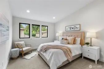 This bedroom exudes warmth and elegance with its soft blush accents, and cozy reading nook. Natural light pours in through large windows, enhancing the serene palette and inviting atmosphere.