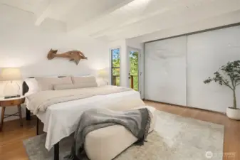 The primary bedroom easily accommodates a king bed and sizeable nightstands, with ample room for bench seating at the foot of the bed.  A large wall of closets spans the wall between the door to the deck on the right and the attached bath just out of frame on the right...